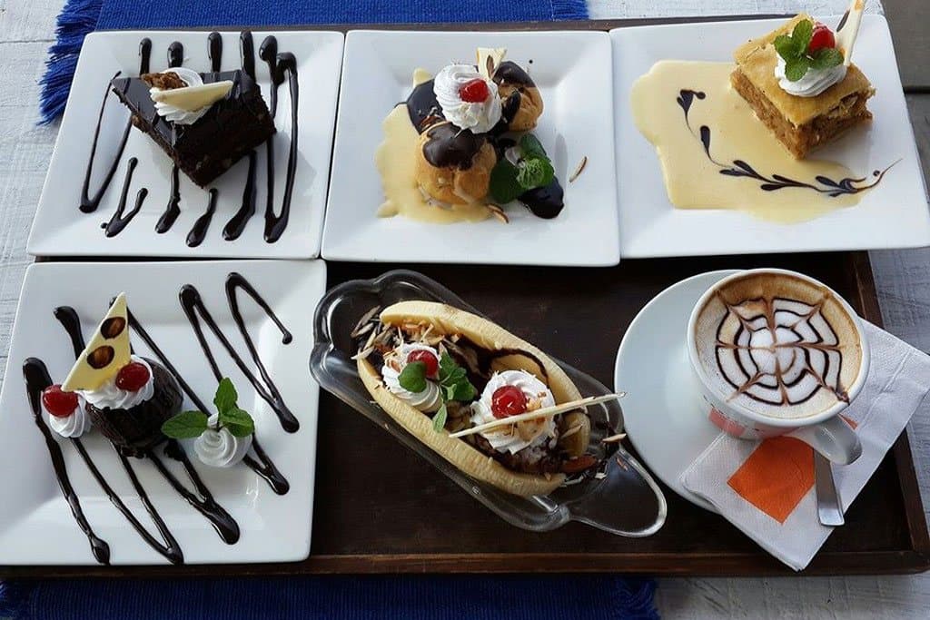 Desserts on white plates: chocolate cake, cream pastries and a cappuccino.