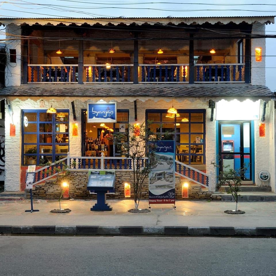 Byanjan’s two-storey front on Barahi Road at dusk: lit windows, blue trim, candles on the steps.