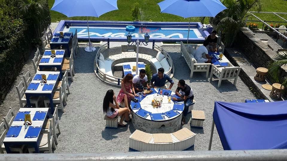 The patio from above: a round table of guests, blue umbrellas and white benches.