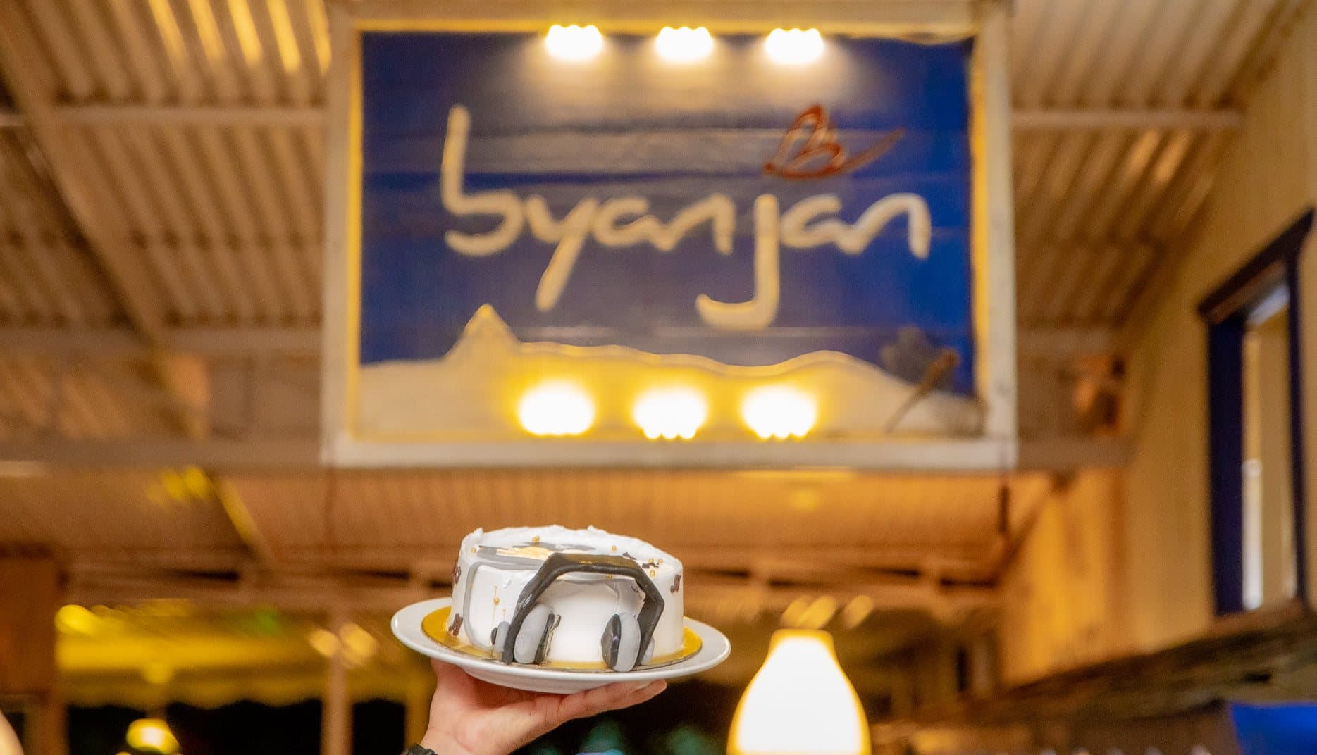 The hand-painted “byanjan” sign with snow peaks, and a cake being carried out beneath it.