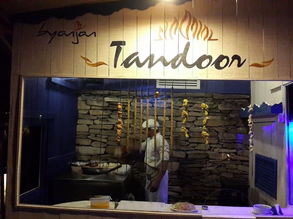 The tandoor kitchen: a stone oven under a carved “Tandoor” sign, a chef at work behind the glass.