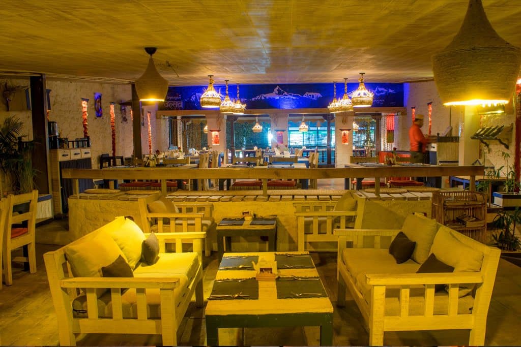 Wooden benches and low tables under lanterns, warm light with blue accents.